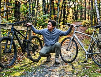 Homme tenant deux vélos sur sentier forestier automnal
